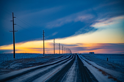 Snow covered highway lined with telephone poles through hills of Montana at sunset. This is central Montana in northwestern United States of America.