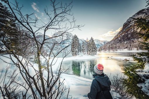 Woman is standing on the coast of mountain lake in winter day