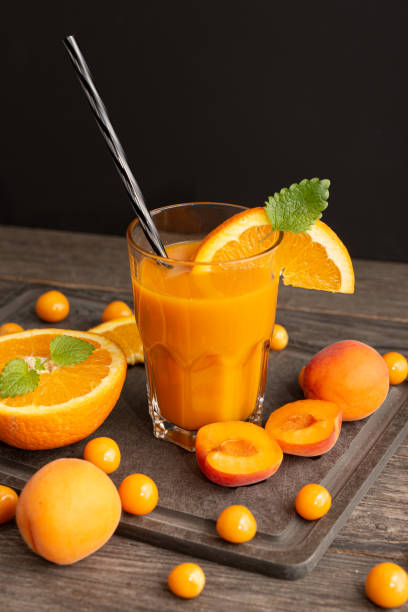 апельсиновый абрикосовый сок в стакане и украшение вокруг на деревянном столе - smoothie fruit orange juice стоковые фото и изображения