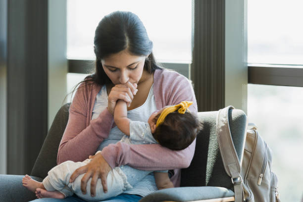 In doctor's waiting room, mother kisses baby's hand As she waits in the psychiatrist's office, the new mom closes her eyes as she kisses her baby's hand. postpartum depression stock pictures, royalty-free photos & images