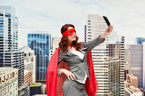 Superhero standing wearing eye mask who is conquering adversity who is taking a selfie and using smart phone