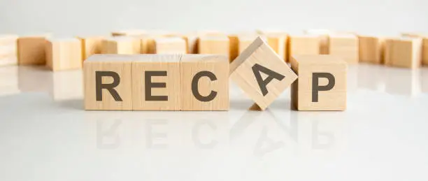 recap - word of wooden blocks with letters on a gray background. reflection of the caption on the mirrored surface of the table.selective focus.