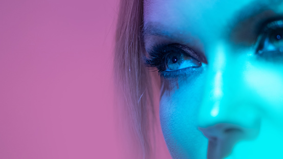 Gaze, eye close-up, young woman in neon blue backlit on pink background