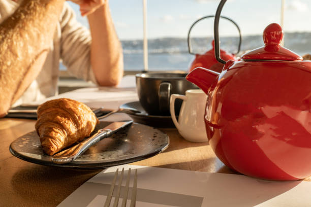 Tea cup and pot with fresh pastries on breakfast table