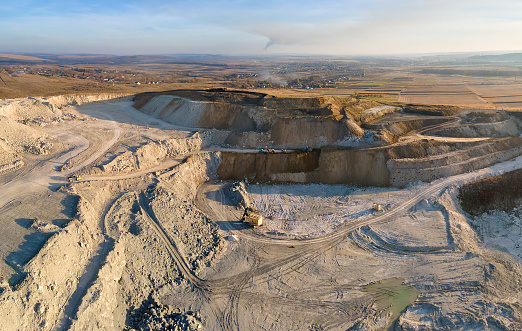 Aerial view of open pit mine of sandstone materials for construction industry with excavators and dump trucks. Heavy equipment in mining and production of useful minerals concept.