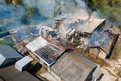 Aerial view of ruined building on fire with collapsed roof and rising dark smoke.