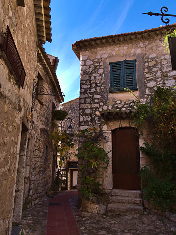 Eze, Provence-Alpes-Cote d'Azur, France - 11-04-2021: Narrow alley in the historic center of small medieval town Eze Village at the French Riviera with old stone buildings on sunny day.