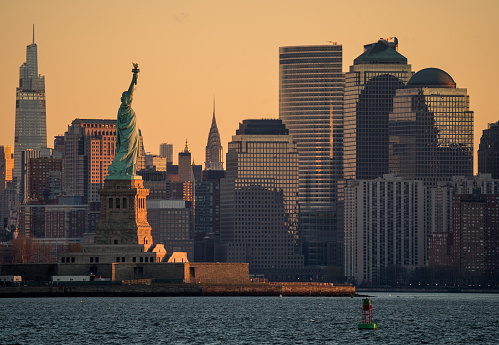 New York, NY - USA -Dec 26, 2021: Horizontal early morning view of the Statue of Liberty in the New York Harbor, with the skyline of lower Manhattan behind her at sunrise.