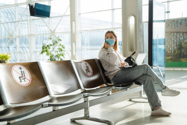 woman in a mask talking on the phone and looking around while sitting on an armchair in the waiting room - airport waiting room waiting airport lounge imagens e fotografias de stock