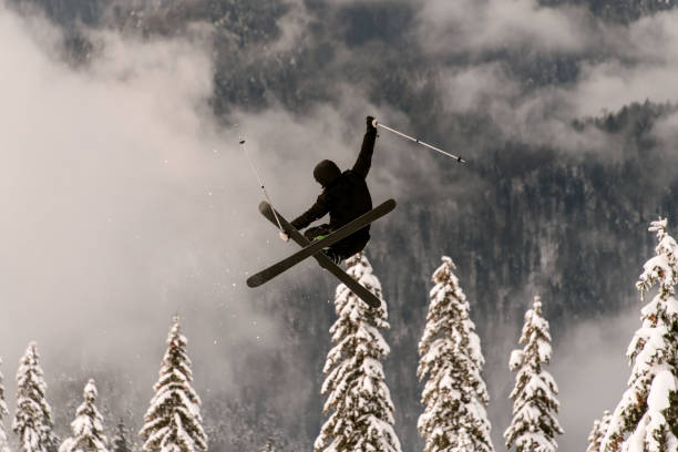 freeride skier performs jump in the air over a snow-covered mountain slope freeride skier performs a masterful jump in the air over a snow-covered mountain slope against a background of snow-covered fir trees extreme skiing stock pictures, royalty-free photos & images