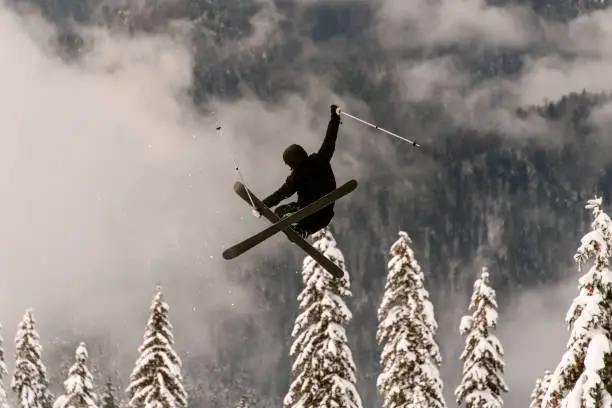 freeride skier performs a masterful jump in the air over a snow-covered mountain slope against a background of snow-covered fir trees