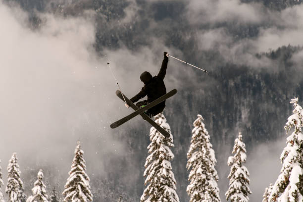 narciarz freeride wykonuje skok w powietrzu nad ośnieżonym zboczem góry - freeride zdjęcia i obrazy z banku zdjęć