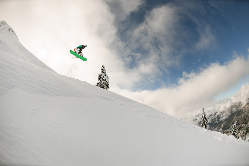 Great view of the snowy mountain slope and the snowboarder jumping air against the background of cloudy sky