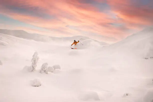 beautiful view of freeride skier in bright jacket skilfully rides on powder snow down the mountain slope against colorful sky in background. Winter sports