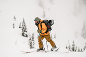 man tourist with skis and trekking poles walks up the hill against the backdrop of snow-covered trees