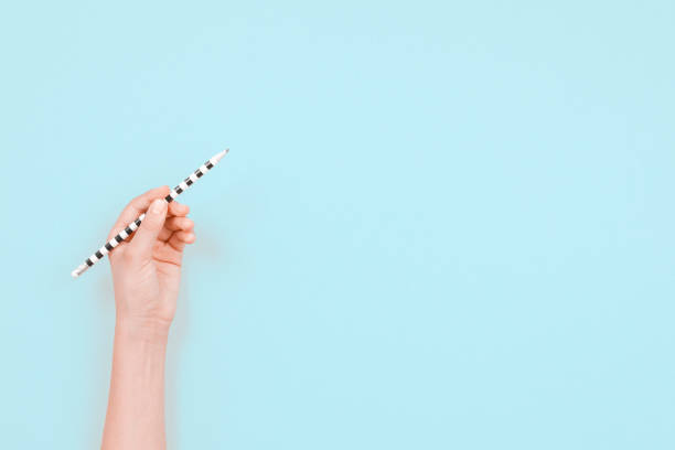 istock Left hand holding pencil for writing over light blue background. Top view, copy space for text. Left Handers Day 1361775428