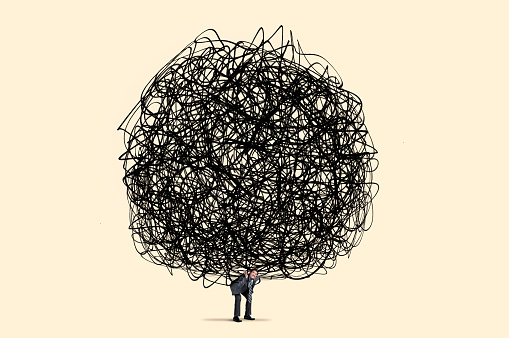 A man carries a large burden, as represented by a large round tangled mess, on his shoulders isolated on a yellow background.\