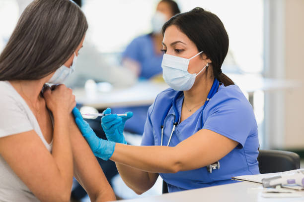 Close up photo female nurse giving vaccine to woman A close up photo of a mid adult female nurse giving a vaccine to an unrecognizable mid adult woman at a vaccination center. booster dose photos stock pictures, royalty-free photos & images