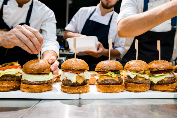 front view of many delicious juicy hamburgers with meat cutlet and vegetables front view of many delicious juicy hamburgers with meat cutlet and vegetables on the table. Hand of chef pierces burger with wooden stick fast food stock pictures, royalty-free photos & images