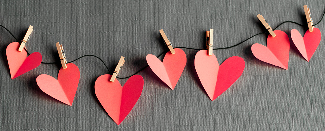 Red paper cut hearts on a clothesline with wooden clothespins. Gray background.