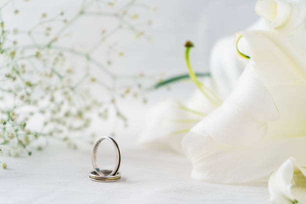 istock A wedding rings on a white surface with beautiful white lilies flowers in the background. Commitment and love concept. Copy space. 1361794656