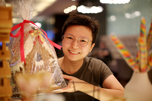 An Asian woman is enjoying choosing gingerbread house for Christmas celebration in Malaysia.