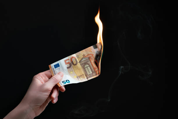 Studio shot of left hand holding a burning fifty Euro bank note. Concept for inflation, eurozone crisis, economic struggle, monetary policy, financial instruments, investment, bear market. stock photo