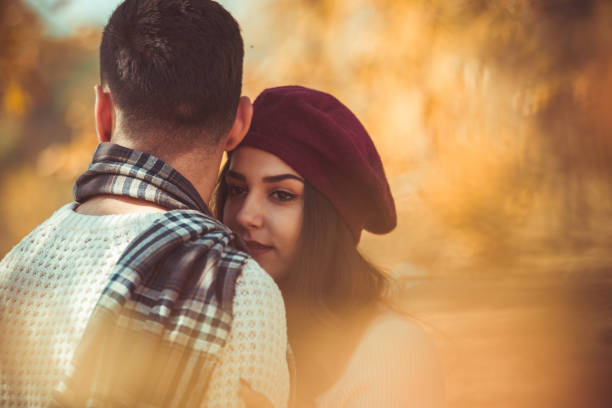 Couple in love is hugging white standing next to the tree, looking happy and satisfied