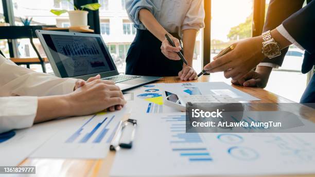 Collaborate At Office Desks To Discuss Paperwork A Financial Group Of Business People Is Meeting To Analyze Data For A Marketing Plan On A Table With Graphs And A Laptop With A Calculator Stock Photo - Download Image Now