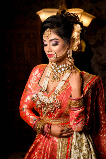 Portrait of very beautiful young Indian bride in luxurious bridal costume with makeup and heavy jewellery in studio lighting indoor. Wedding Fashion and Lifestyle. stock photo