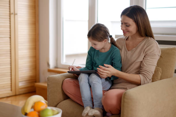 istock Smiling mother and cute daughter using tablet computer together at home 1361836361