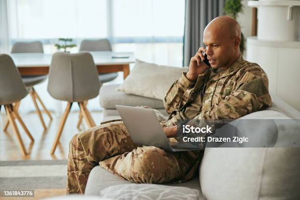 Black Military Man Using Laptop While Talking On The Phone At Home Stock Photo - Download Image Now