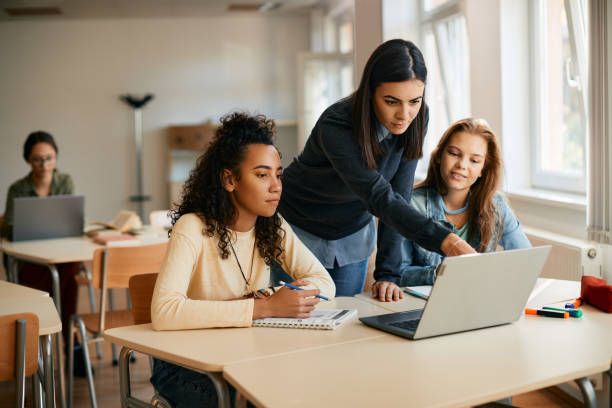 High school professor assisting her students in e-learning on laptop in the classroom. IT teacher and her students using laptop during computer class in high school. instructor stock pictures, royalty-free photos & images