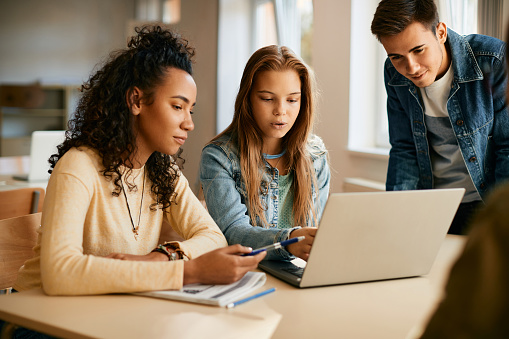 Multiracial group of teenagers using laptop while studying on computer class in high school.