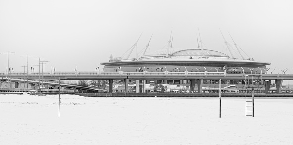 View of the Gazprom Arena stadium from the embankment of the 300th Anniversary Park of St. Petersburg. Football Alley 1, St. Petersburg, Russia. December 19, 2021. Black and white photo.