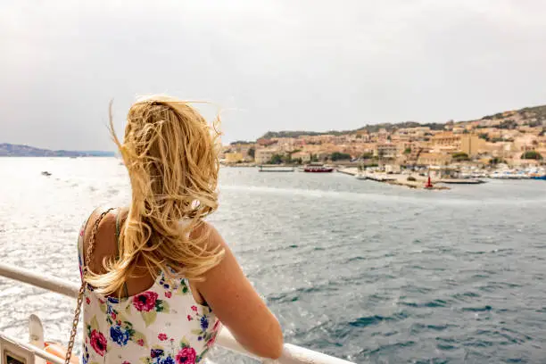 Photo of Blonde woman looking a small town from the cruise ship, Maddalena island, Sardinia, Italy.