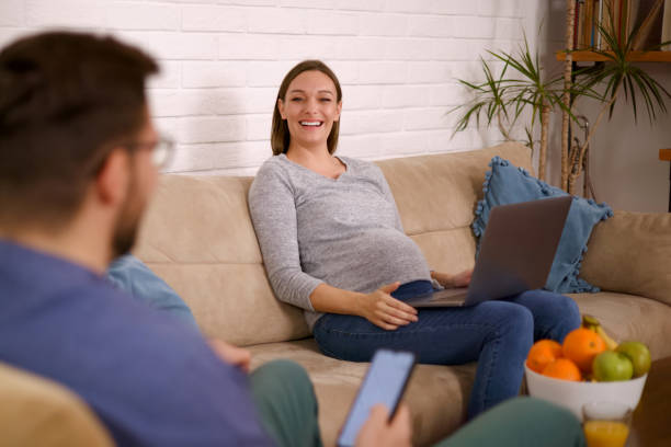 istock Pregnant couple staying at home enjoying surfing the web using various technology devices 1361848903