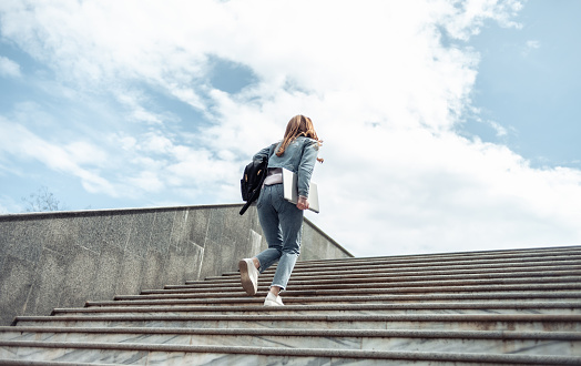 Young woman student climbs the stairs up