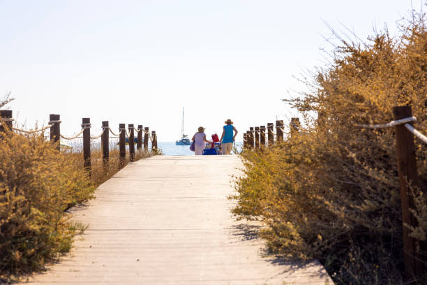 View of senior tourists walking on the path on the beach, Sardinia, Italy.