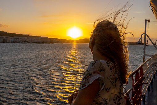 View of a woman looking at the sea during sunset from a cruise ship deck, Sardinia, Italy.