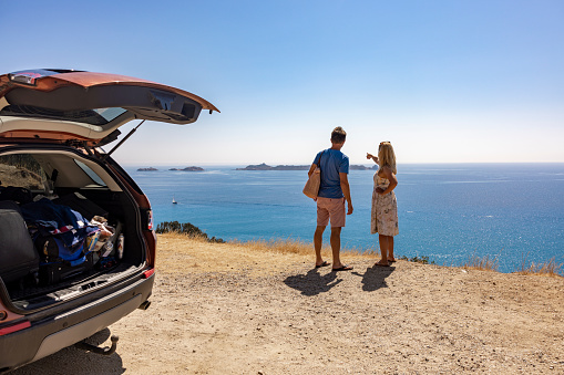 View of a couple with the car along the coast facing the Mediterranean sea, Sardinia, Italy.