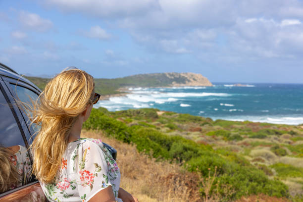 View of a blonde woman with sunglasses looking the coastline in Sardinia, Italy.