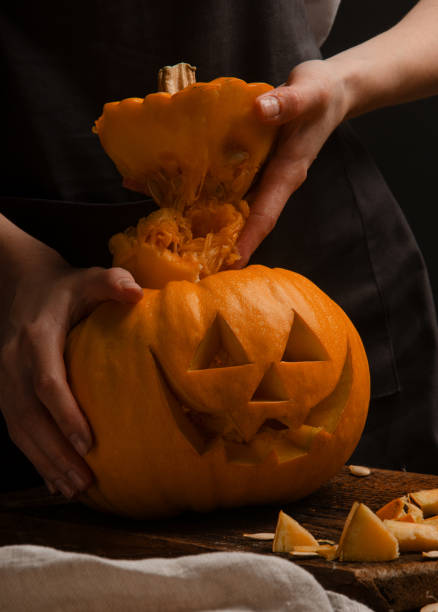 istock Hands cutting, carving pumpkin into jack-o-lanterns for halloween close up. 1361862533