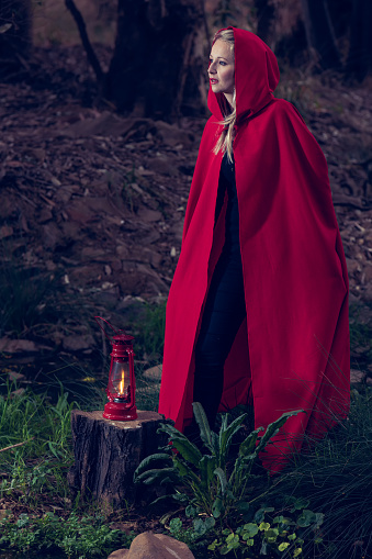 Attractive woman dressed a little red riding-hood walk in a dark forest with a lantern