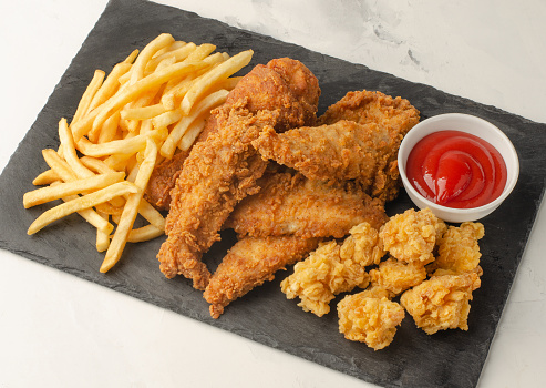 French fries and chicken nuggets and strips meal on a black stone cutting board