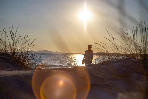 View of a woman walking on the beach with sunlight in background, Sardinia, Italy.