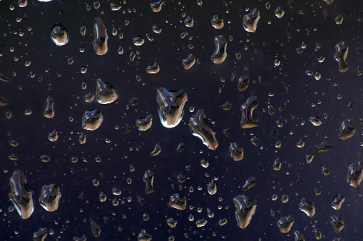 Drops of rain on glass against blue sky and white clouds.