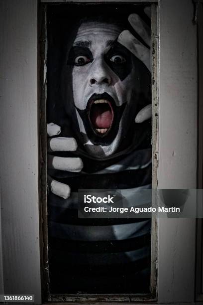 Vertical Terrifying Shot Of A Male In A Mime Costume Posing In Horror Behind The Window Of An Old Rusty Door Stock Photo - Download Image Now