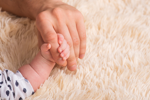 Papá sostiene en sus manos una pequeña mano de bebé. Mano pequeña de un bebé recién nacido en manos grandes de papá. El bebé sostiene el dedo del padre photo