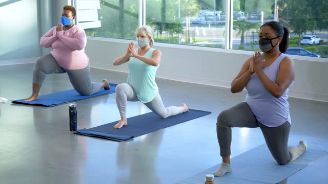 Women in yoga class do crescent lunge with prayer hands